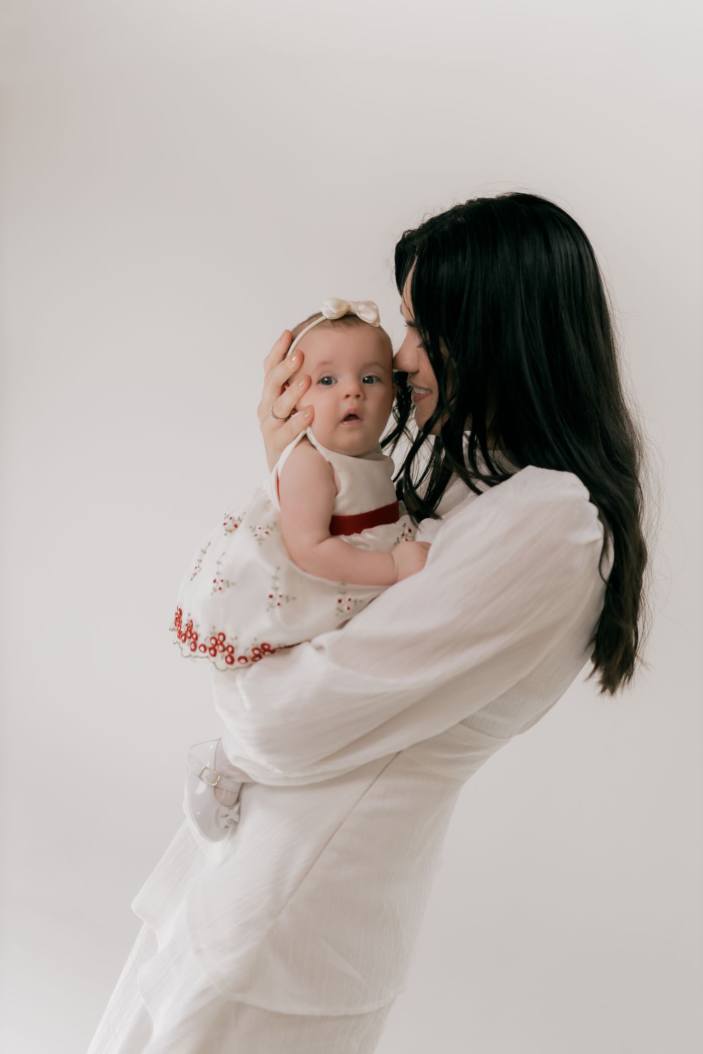 Jeune maman en robe blanche tenant son bébé dans ses bras dans une ambiance douce