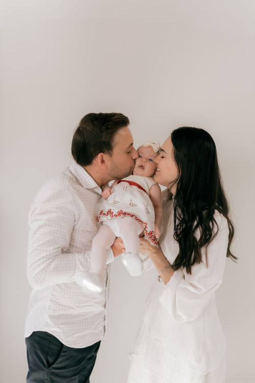 Free Parents lovingly kissing their newborn baby in a heartwarming family portrait. Stock Photo