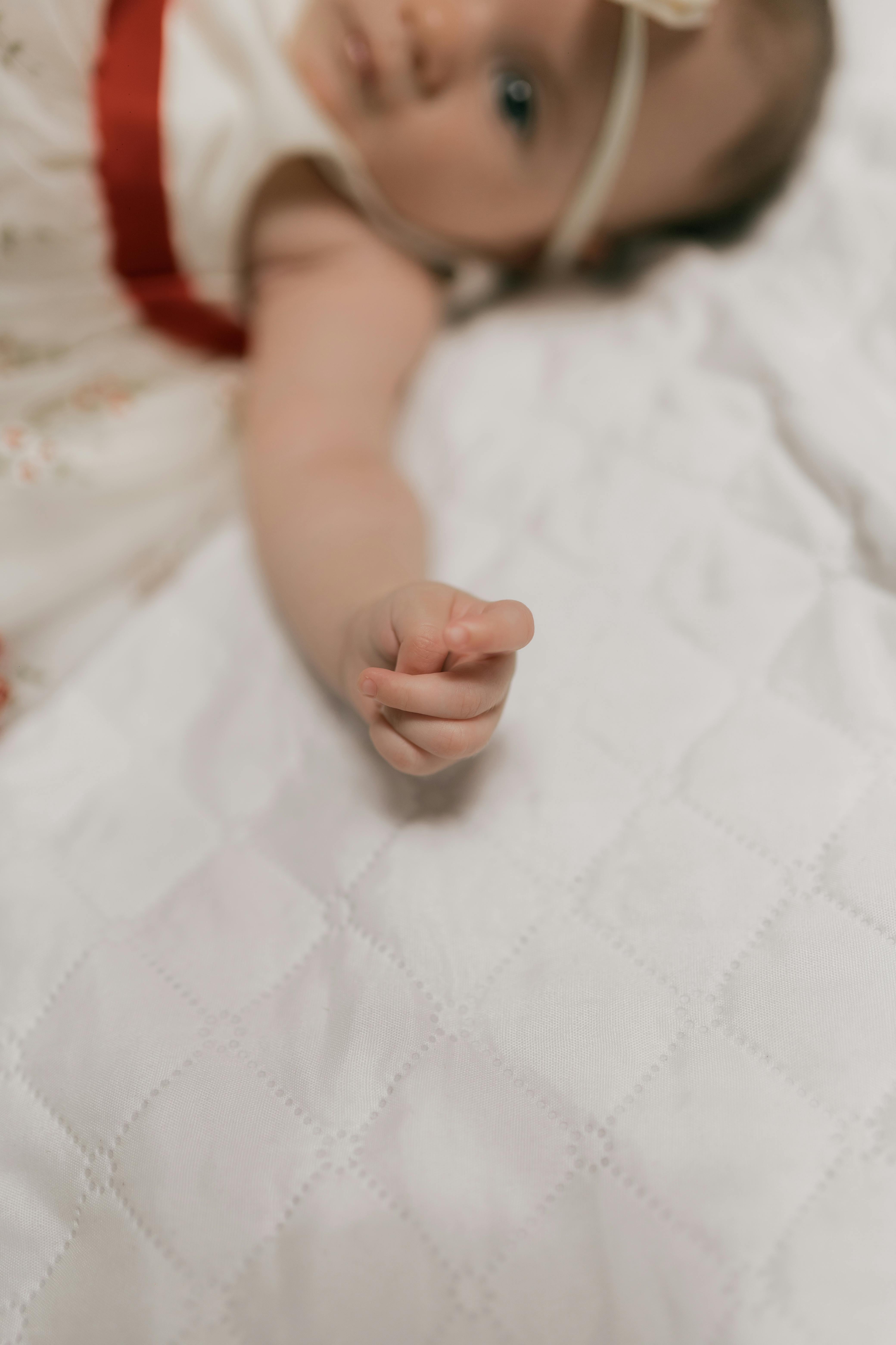 A cozy scene of a baby's hand reaching out on a soft white blanket.