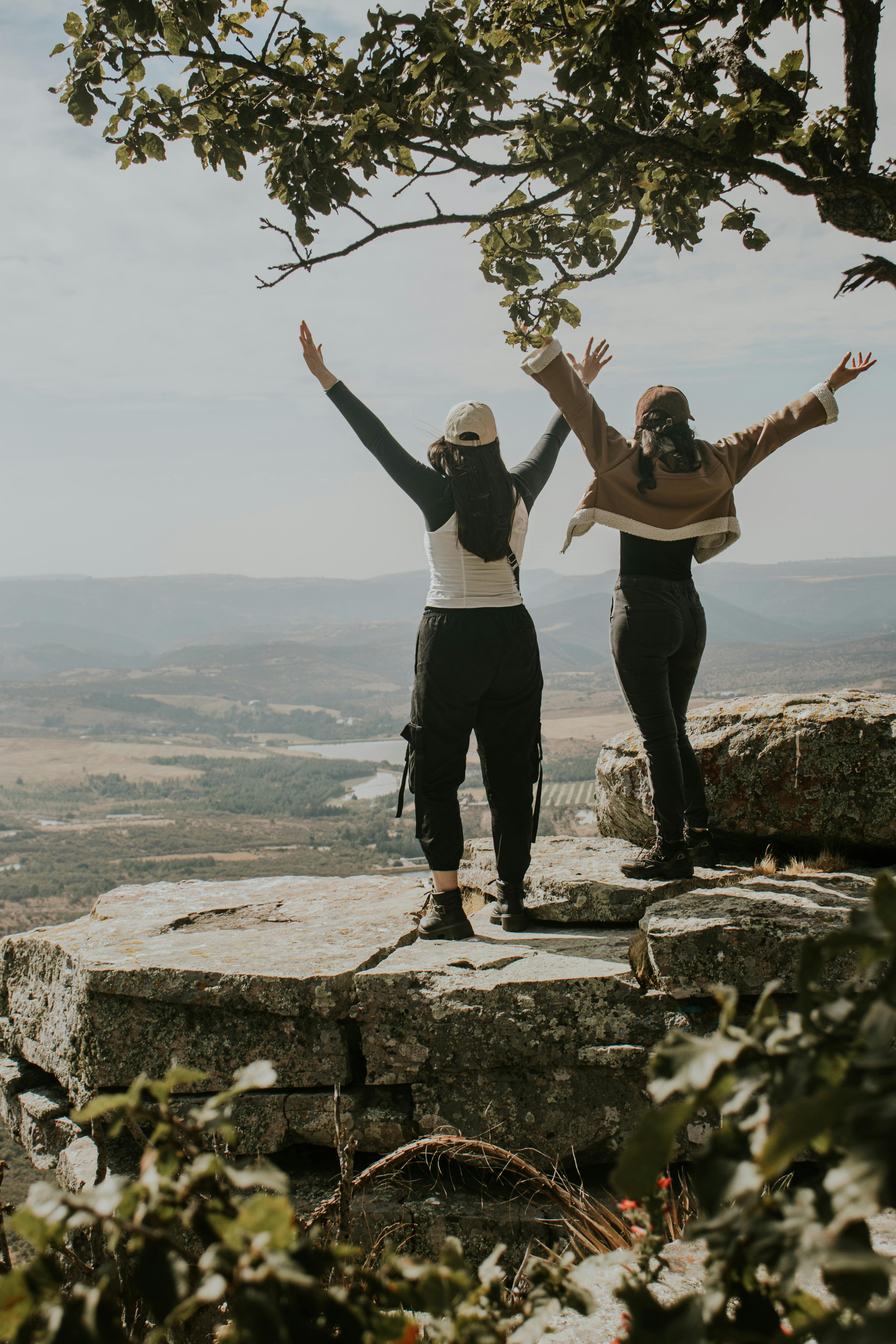 两名女子高举双臂，站在风景秀丽的岩石山崖上，庆祝胜利。