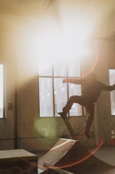 Skateboarder executing a trick indoors, bathed in dramatic sunlight.
