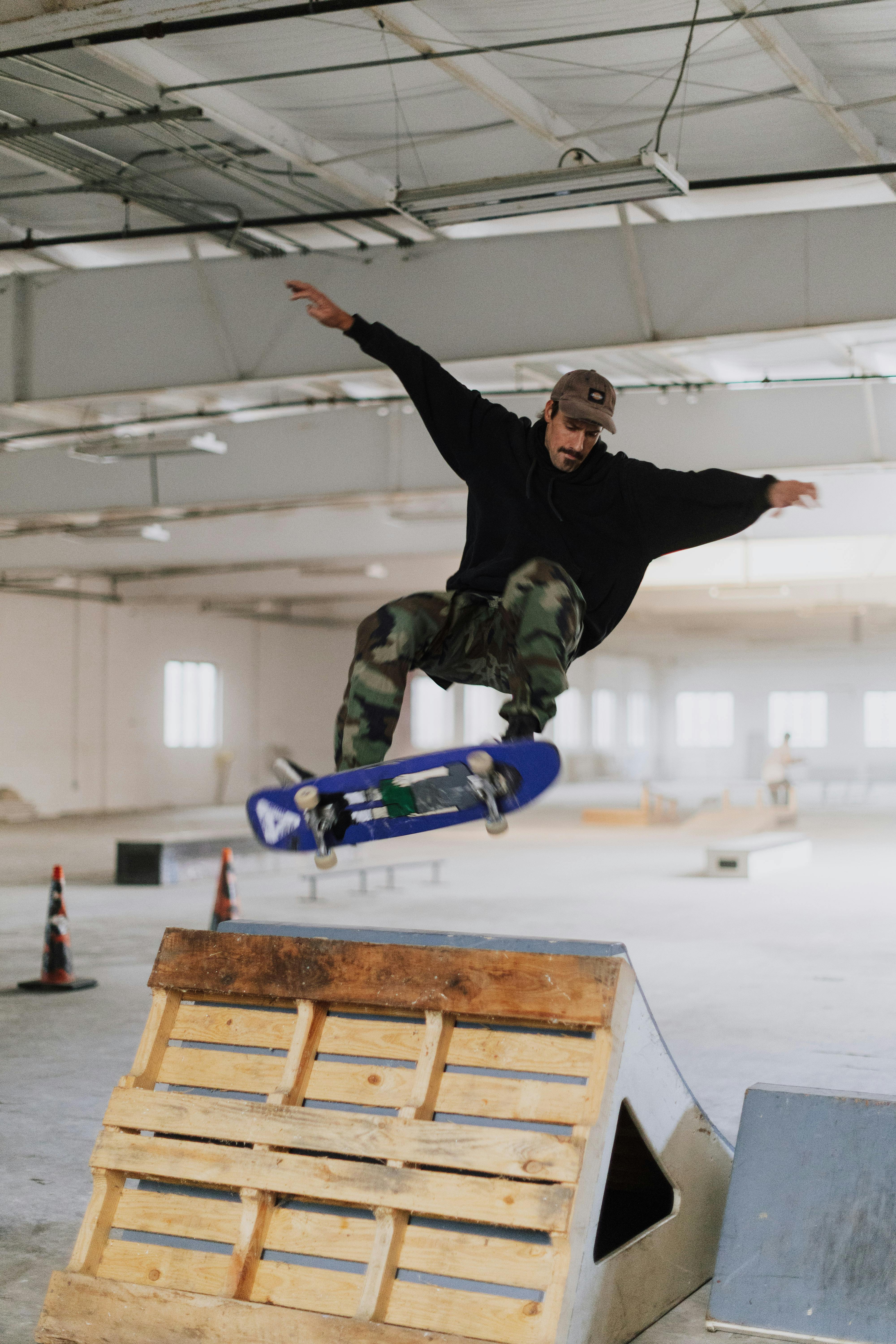 Man performing a skateboarding trick indoors in a spacious skate park.
