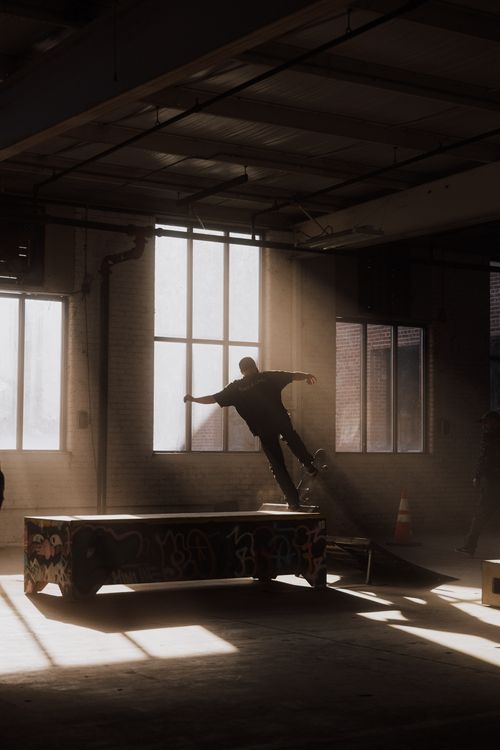 Free A skateboarder performs tricks indoors under dramatic sunlight, urban and energetic setting. Stock Photo