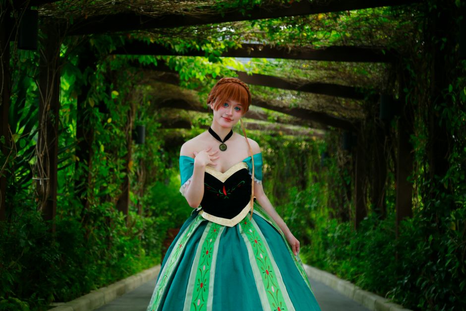 Woman in a detailed costume standing in a lush, verdant tunnel.