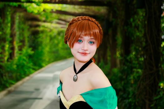 Beautiful costume portrayal in a vibrant green dress surrounded by lush outdoor greenery.