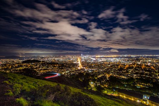 Breathtaking night view of a sprawling cityscape from a hilltop with vibrant city lights and dynamic clouds.