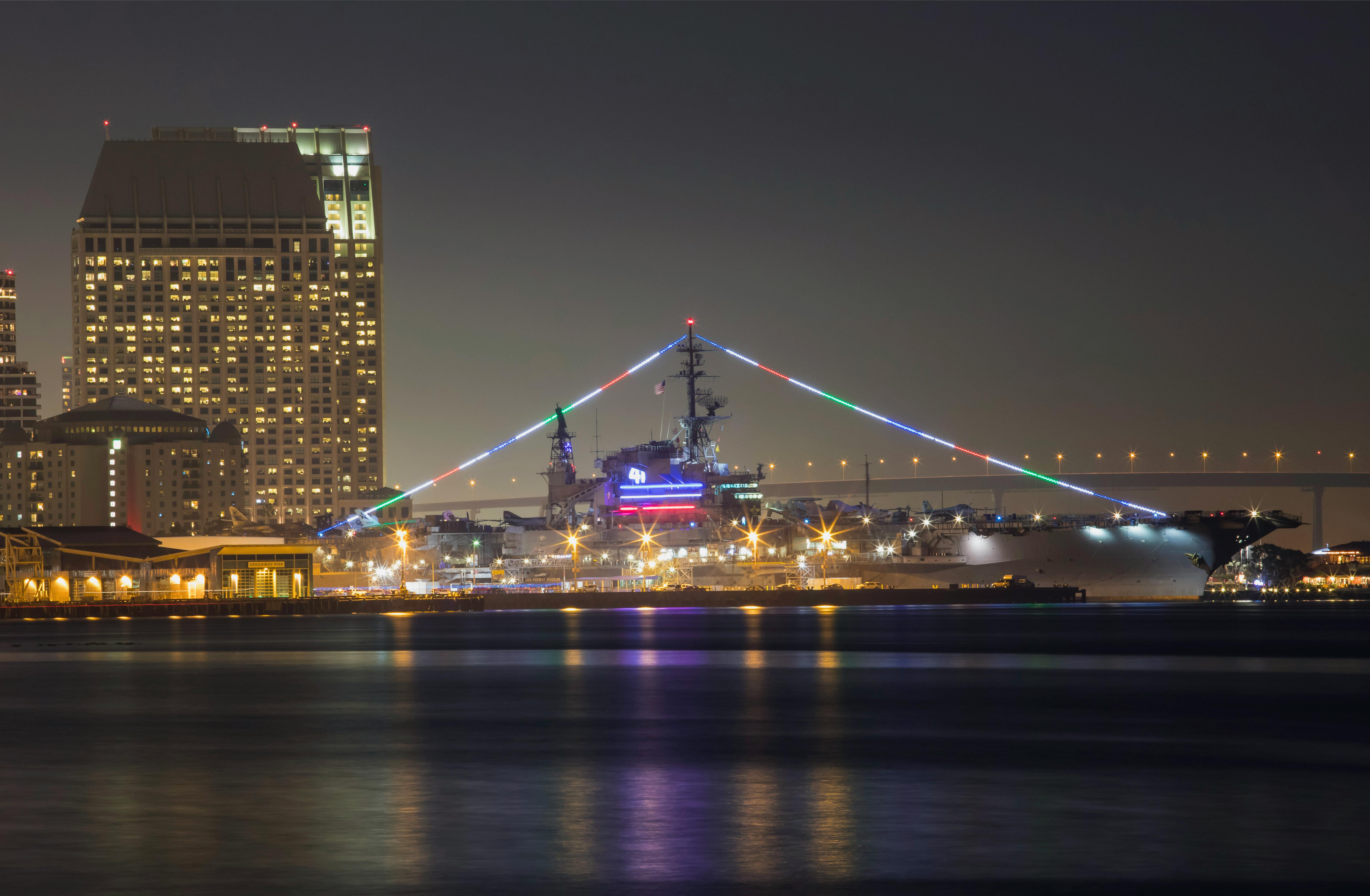 Night view of USS Midway Museum with city skyline, colorful lights in San Diego.