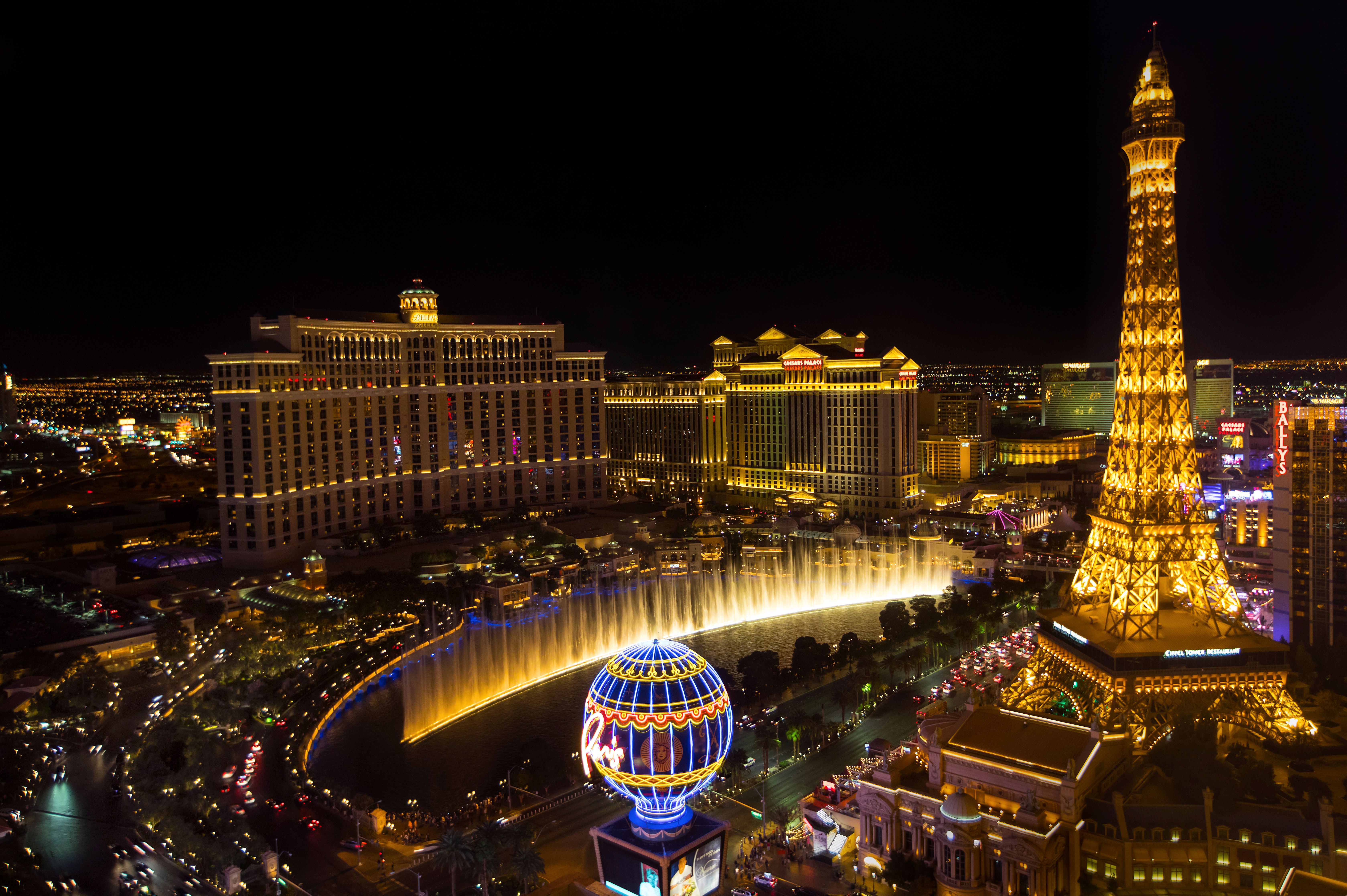 Stimmungsvolle Nachtansicht nahe der Springbrunnen Des Bellagio in Las Vegas, Vereinigte Staaten, mit dem Eiffelturm von Paris Las Vegas und den Lichtern des Strip hinter den Brunnen.