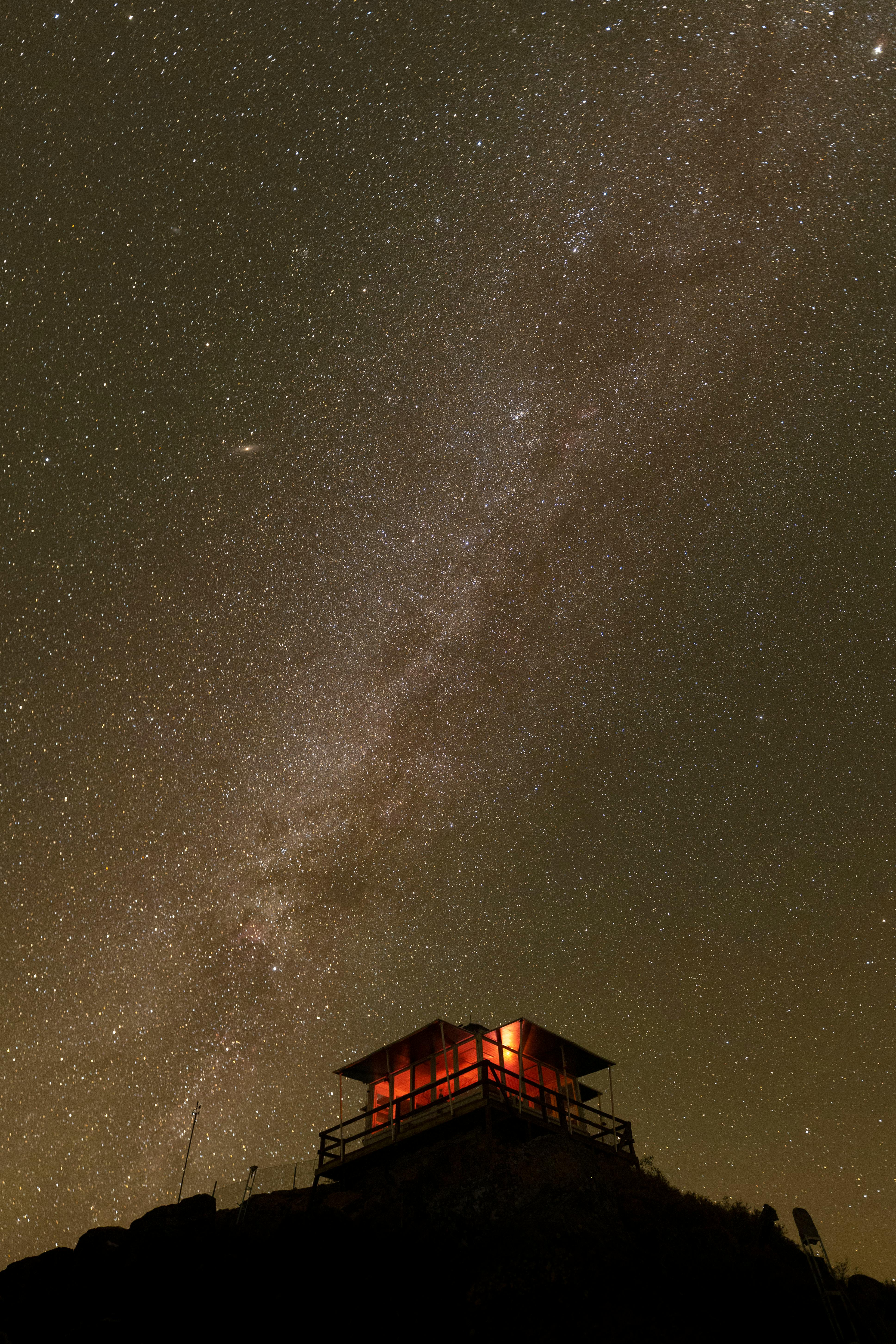 A mesmerizing view of a starry sky with a remote cabin illuminated at night.