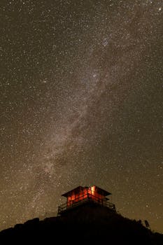 A mesmerizing view of a starry sky with a remote cabin illuminated at night.