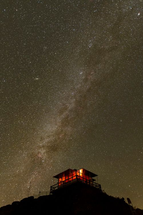 Free A stunning view of the Milky Way over a lit cabin at night, against a star-filled sky. Stock Photo