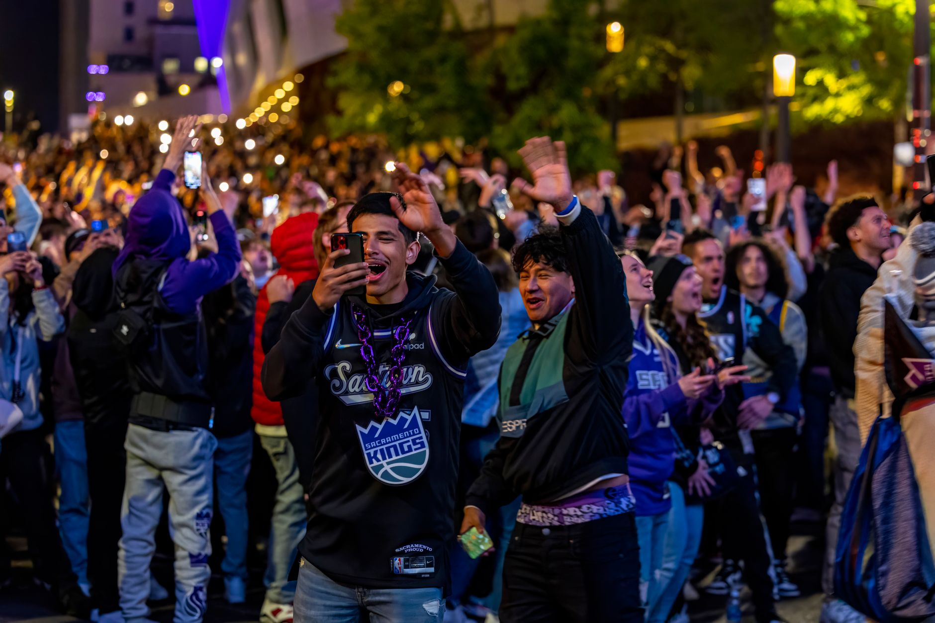 Energetic crowd celebrating outdoors at night, capturing exciting moments with smartphones.