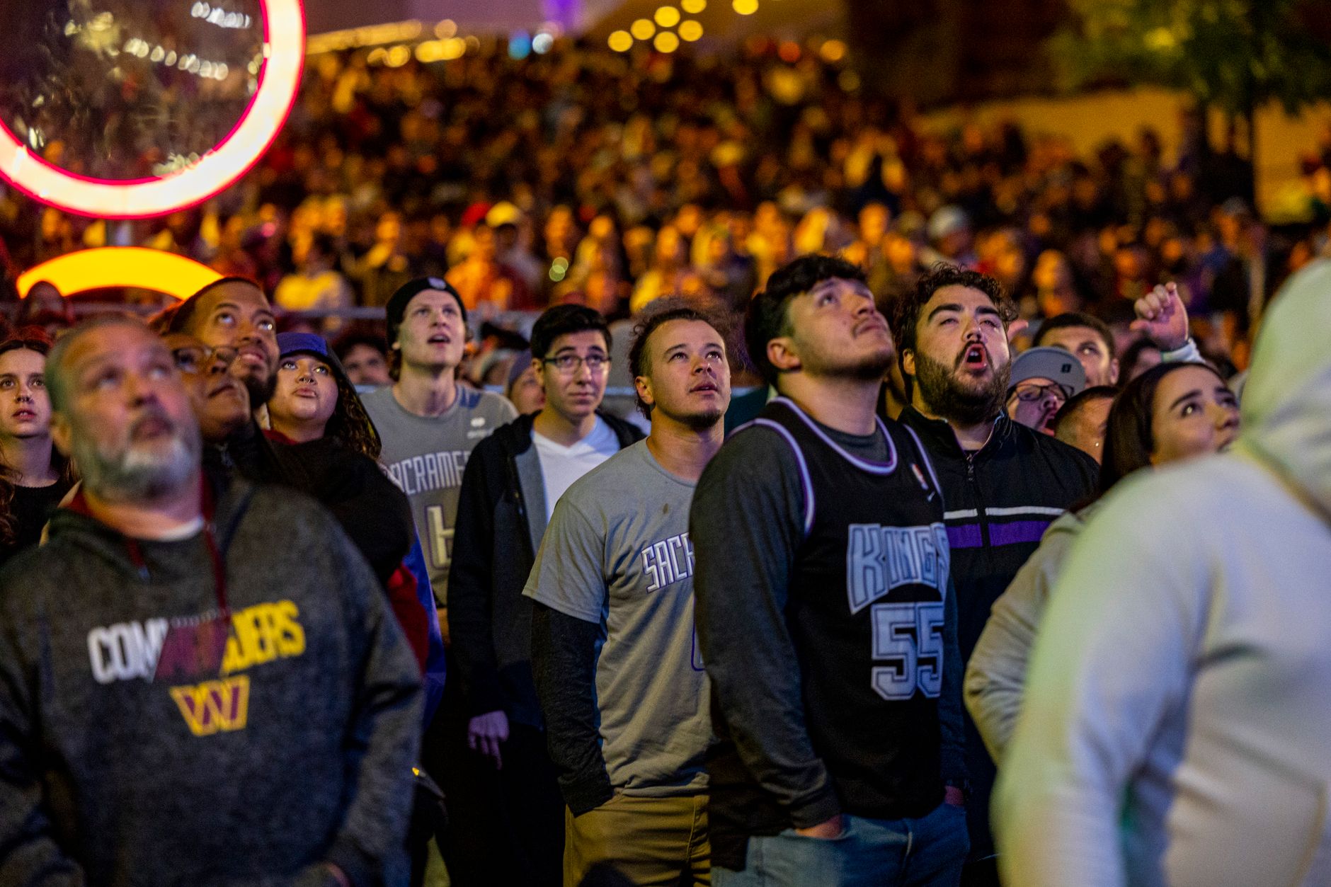 A diverse crowd gathers at night, watching a sports event with rapt attention.