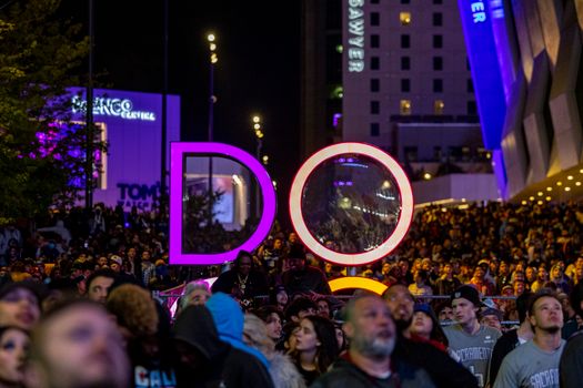 A lively crowd gathers at an outdoor nighttime event with bright signage.
