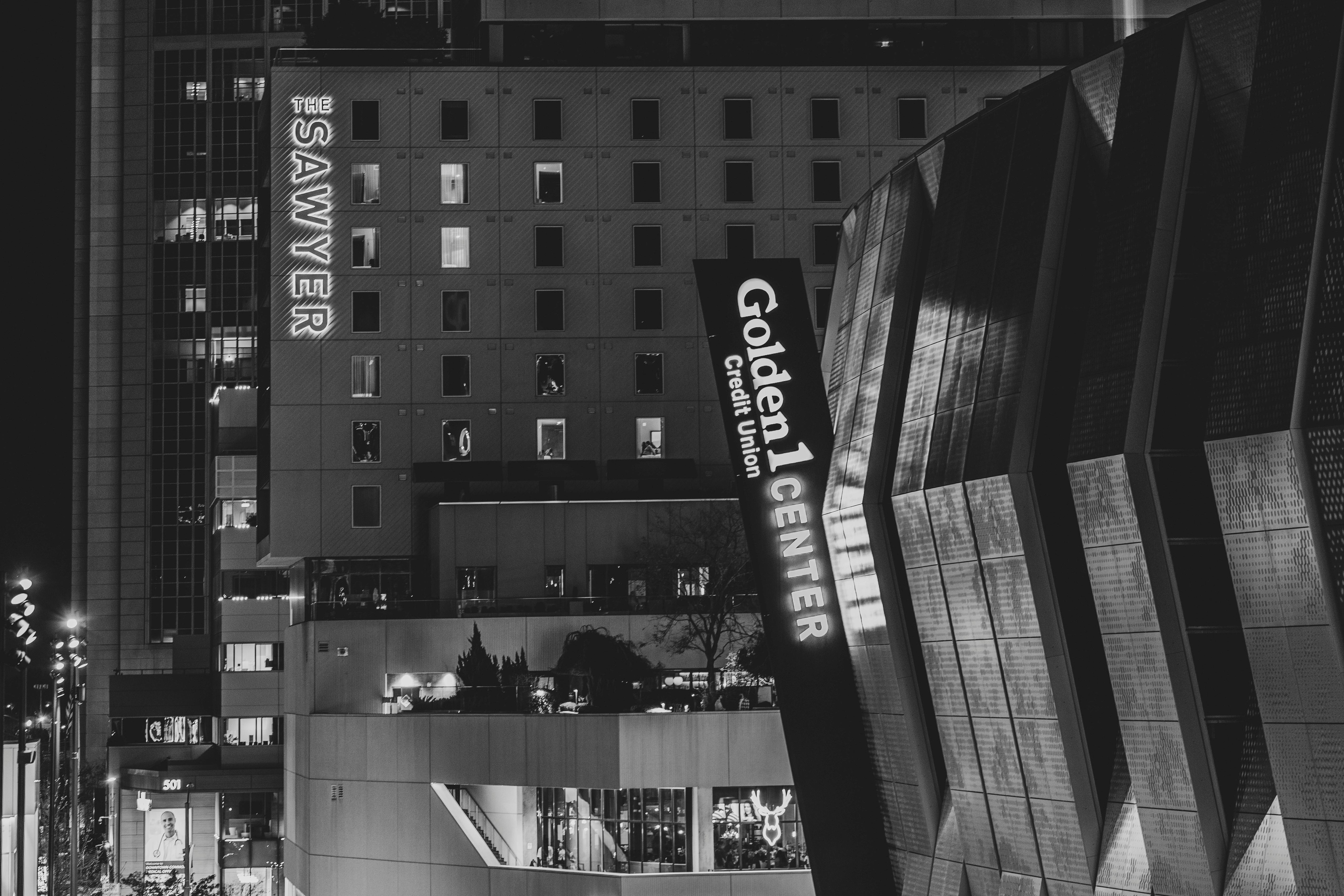 Ücretsiz Gece vakti şehir ortamında Golden 1 Center ve Sawyer Hotel'in siyah beyaz fotoğrafı. Stok Fotoğraflar