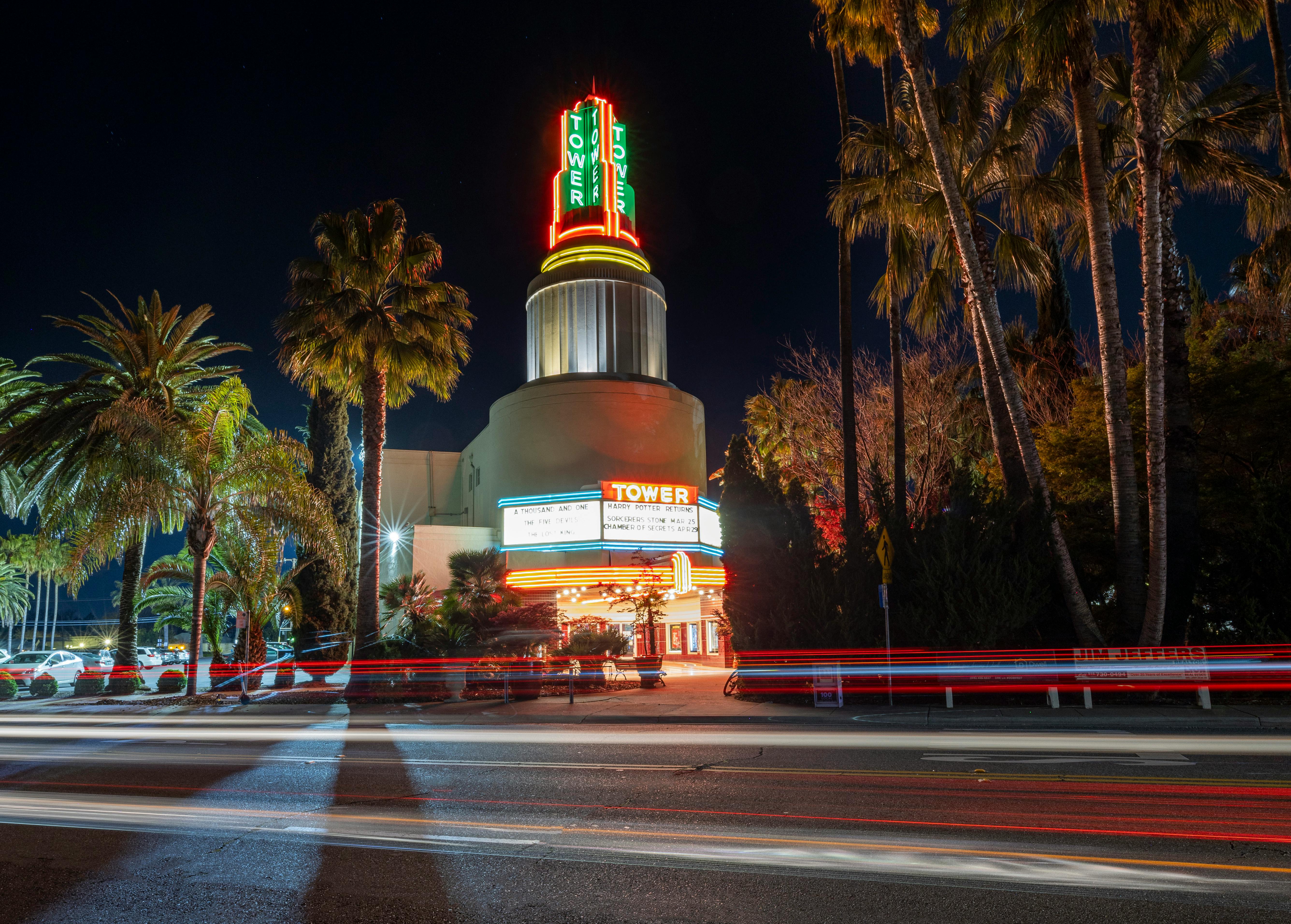 Free Night view of an iconic theater illuminated with neon lights, surrounded by palm trees. Stock Photo