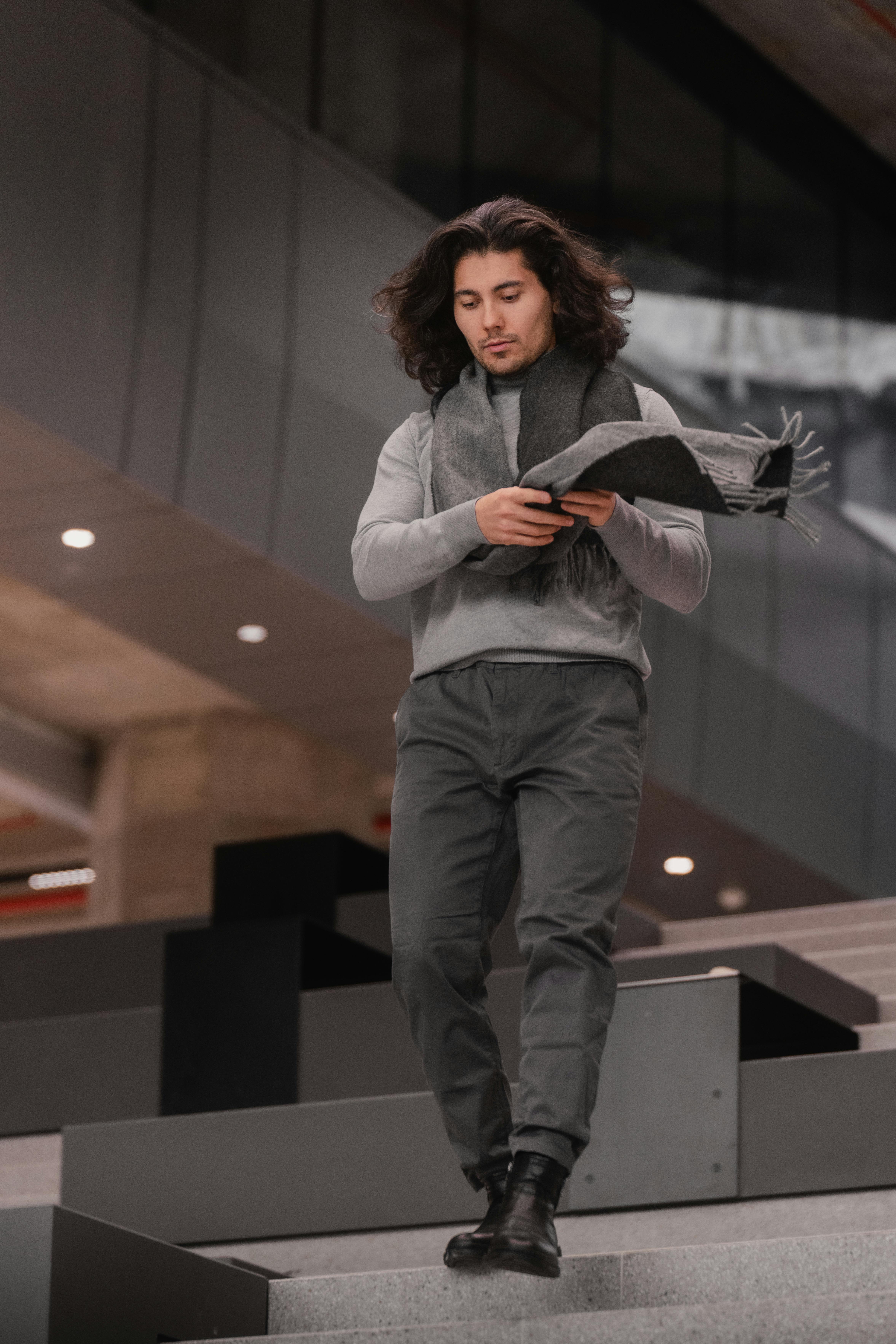 Kostenlos Ein modisch gekleideter Mann mit langen Haaren steigt in einer modernen urbanen Umgebung eine Treppe hinunter. Stock-Foto