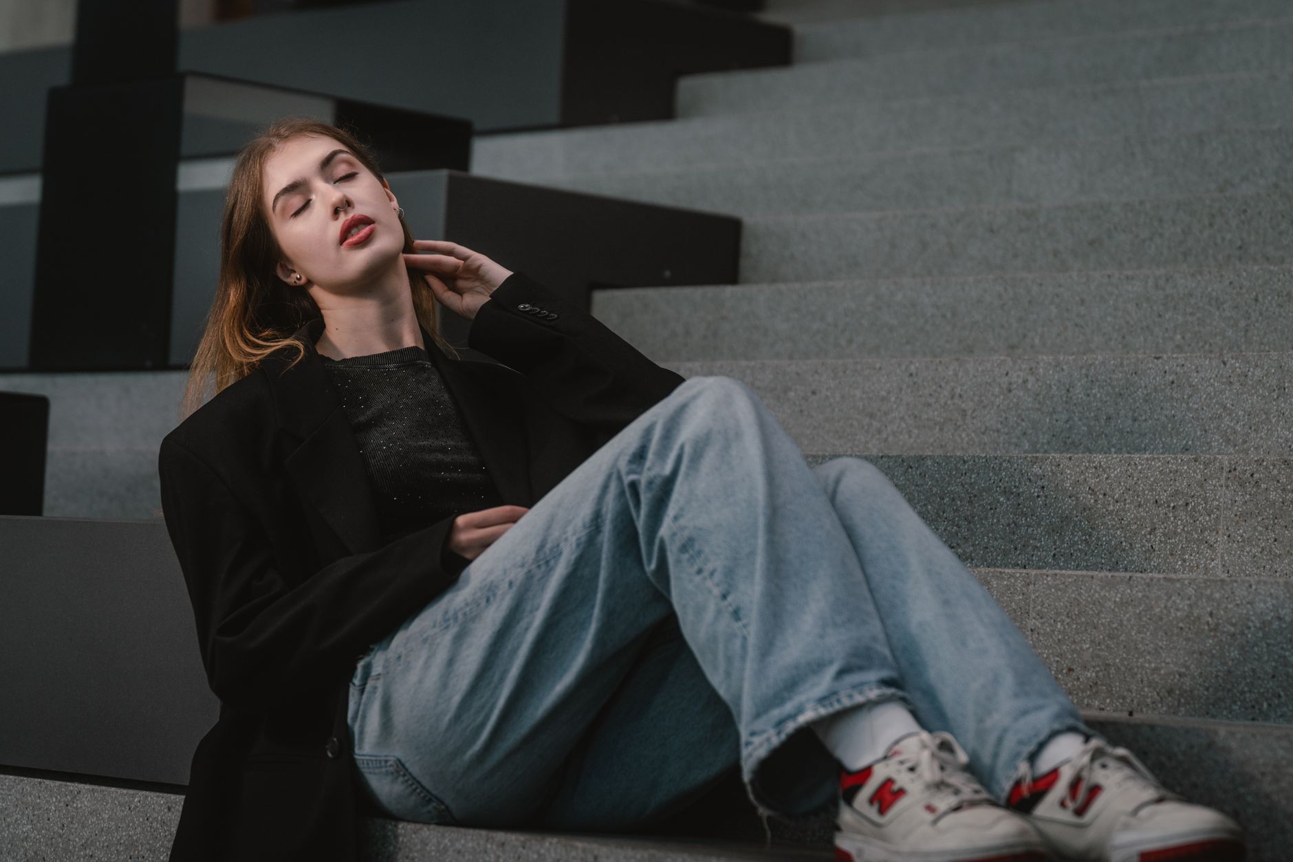 Stylish young woman in urban setting, relaxed on modern steps in Vienna.