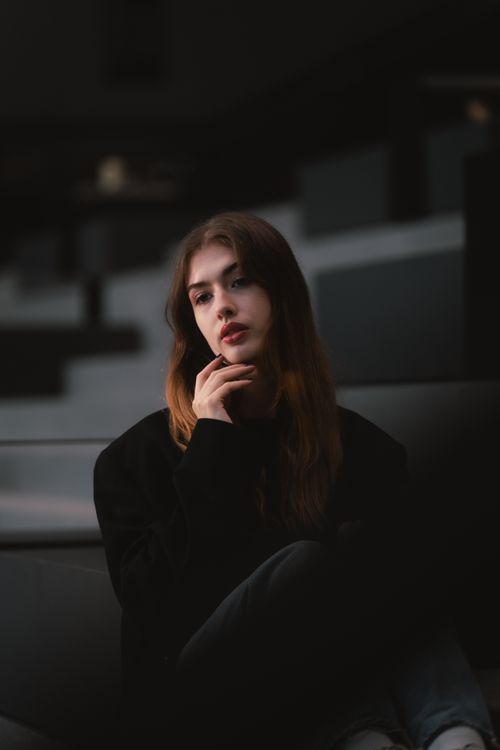 Free Moody portrait of a young adult woman sitting thoughtfully in a city environment. Stock Photo