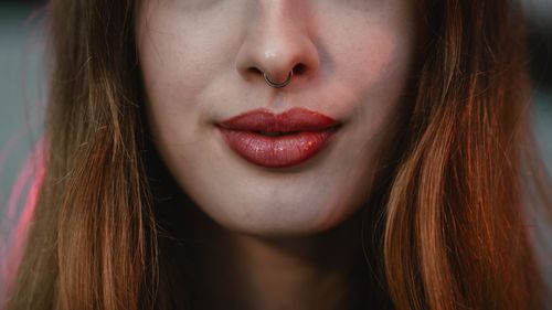 Free A focused close-up portrait of a young woman with red lipstick and a nose ring against a soft background. Stock Photo