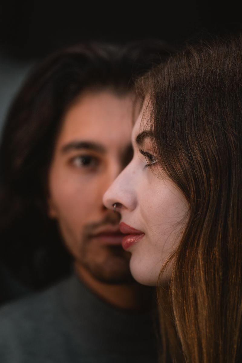 Intriguing close-up portrait of a young couple against a dark background, featuring a thoughtful and intimate expression.
