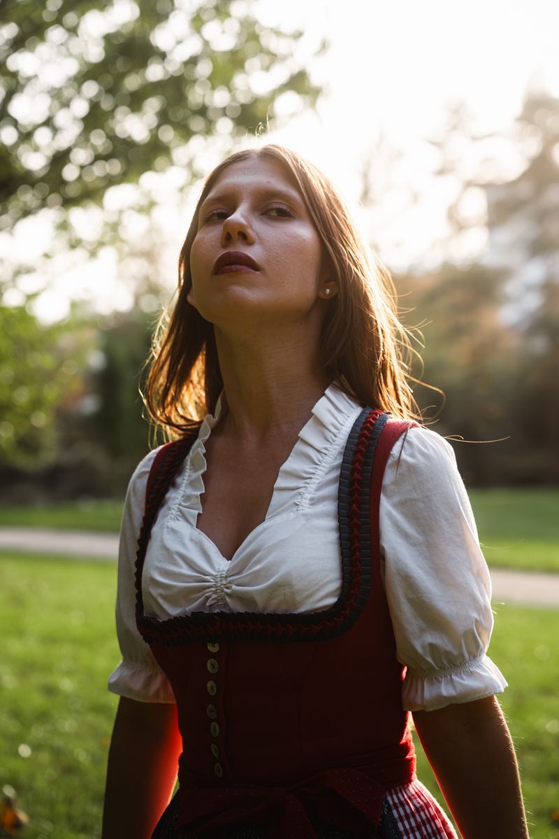 A woman wearing a traditional dirndl dress stands outdoors in the warm glow of fall.
