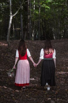 Two women holding hands in traditional dress in a serene Austrian forest.