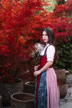 Young woman in Austrian folk costume amidst vibrant autumn leaves in Graz, Austria.