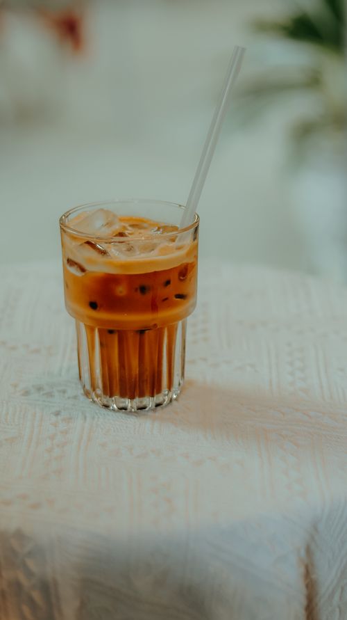 Free A refreshing glass of iced coffee with a straw on a textured white tablecloth, perfect for summer days. Stock Photo