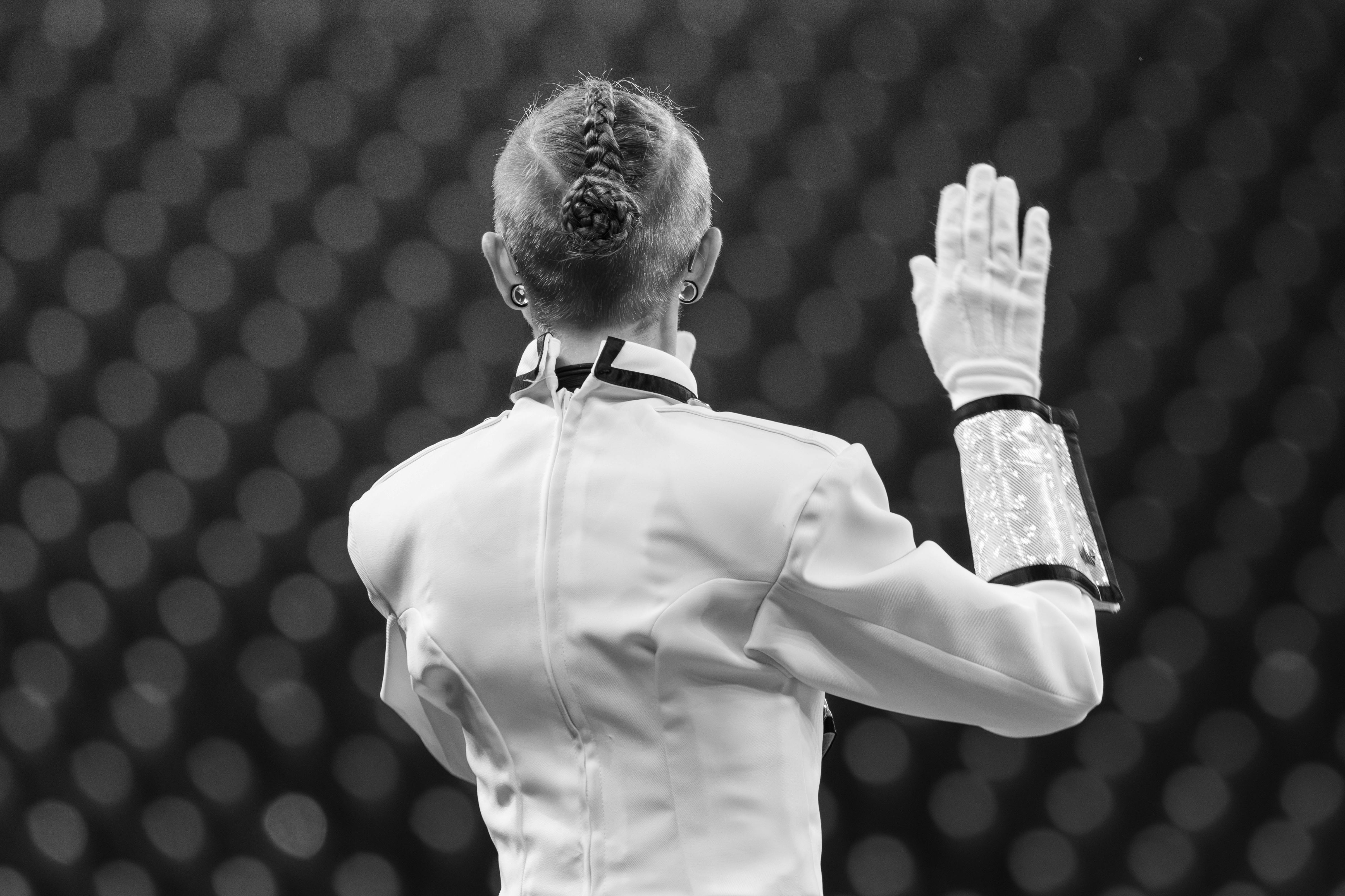 A conductor leading an orchestra from behind, wearing a uniform and glove.