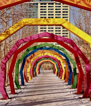 Vibrant rainbow archway in a snowy urban setting, leading to a city building.