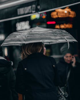 City street with a woman holding an umbrella on a rainy day, capturing urban life.