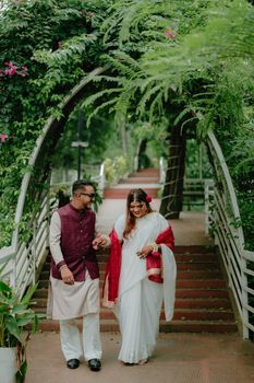 A happy couple in traditional attire walking under a green archway at a lush outdoor setting.