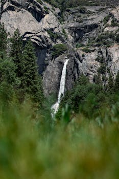 Stunning view of a waterfall in the rocky landscape of California, surrounded by lush green forest.