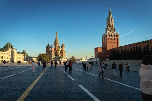 Crowds enjoying a sunny day at Moscow's iconic Red Square, featuring St. Basil's Cathedral and Spasskaya Tower.