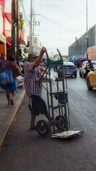 A street vendor maneuvering a cart on a bustling city street filled with cars and pedestrians.