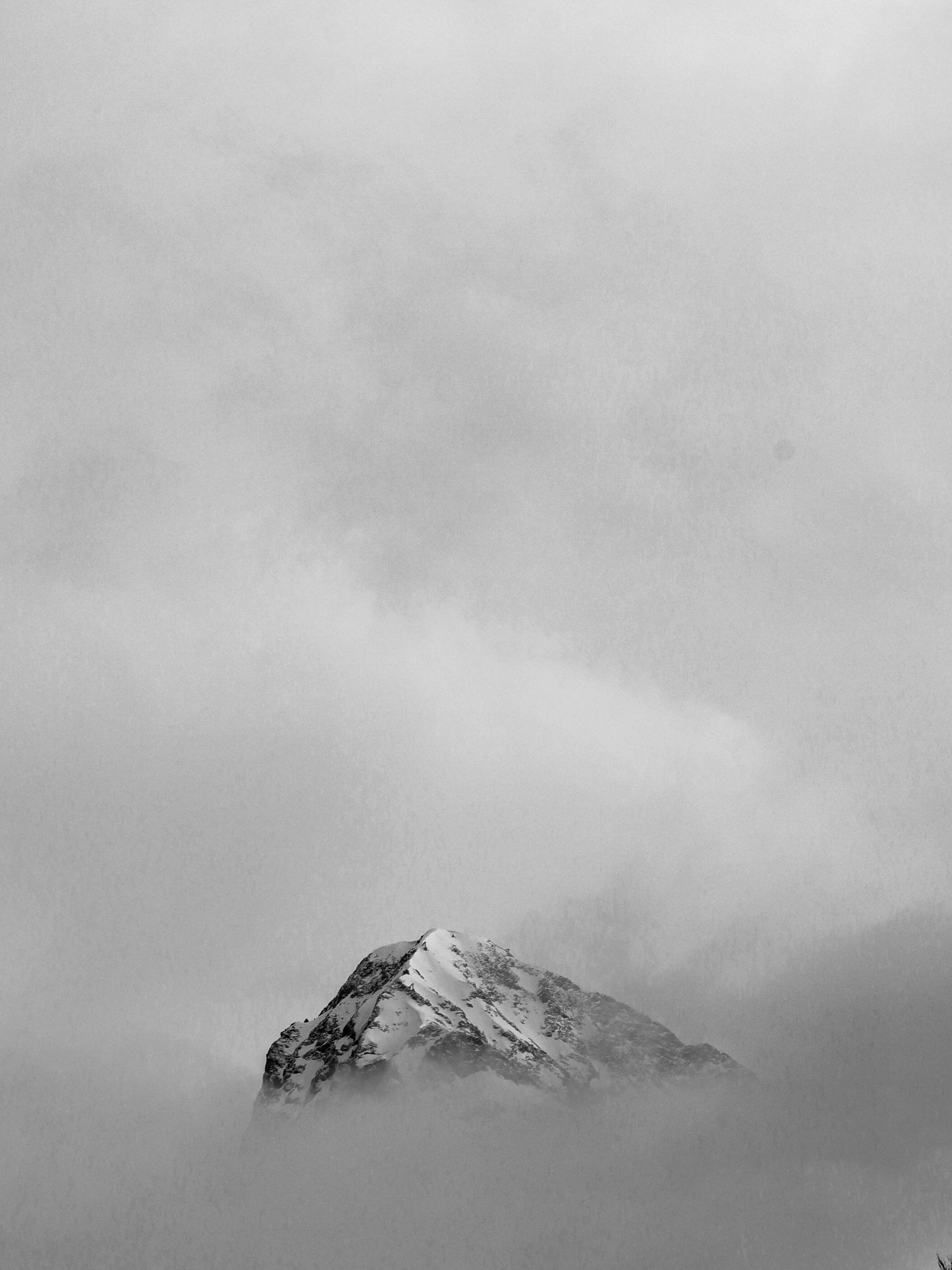A dramatic view of a snow-covered mountain peak surrounded by misty clouds in black and white.