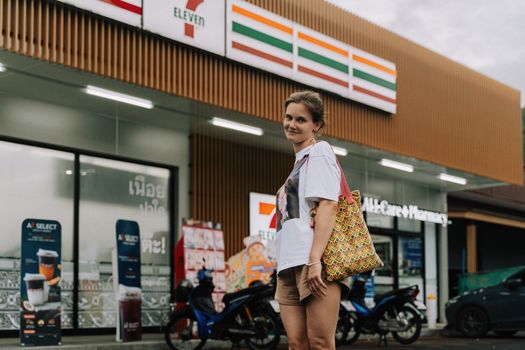 A woman standing in front of a 7-Eleven store in Phuket, Thailand, with a casual pose.