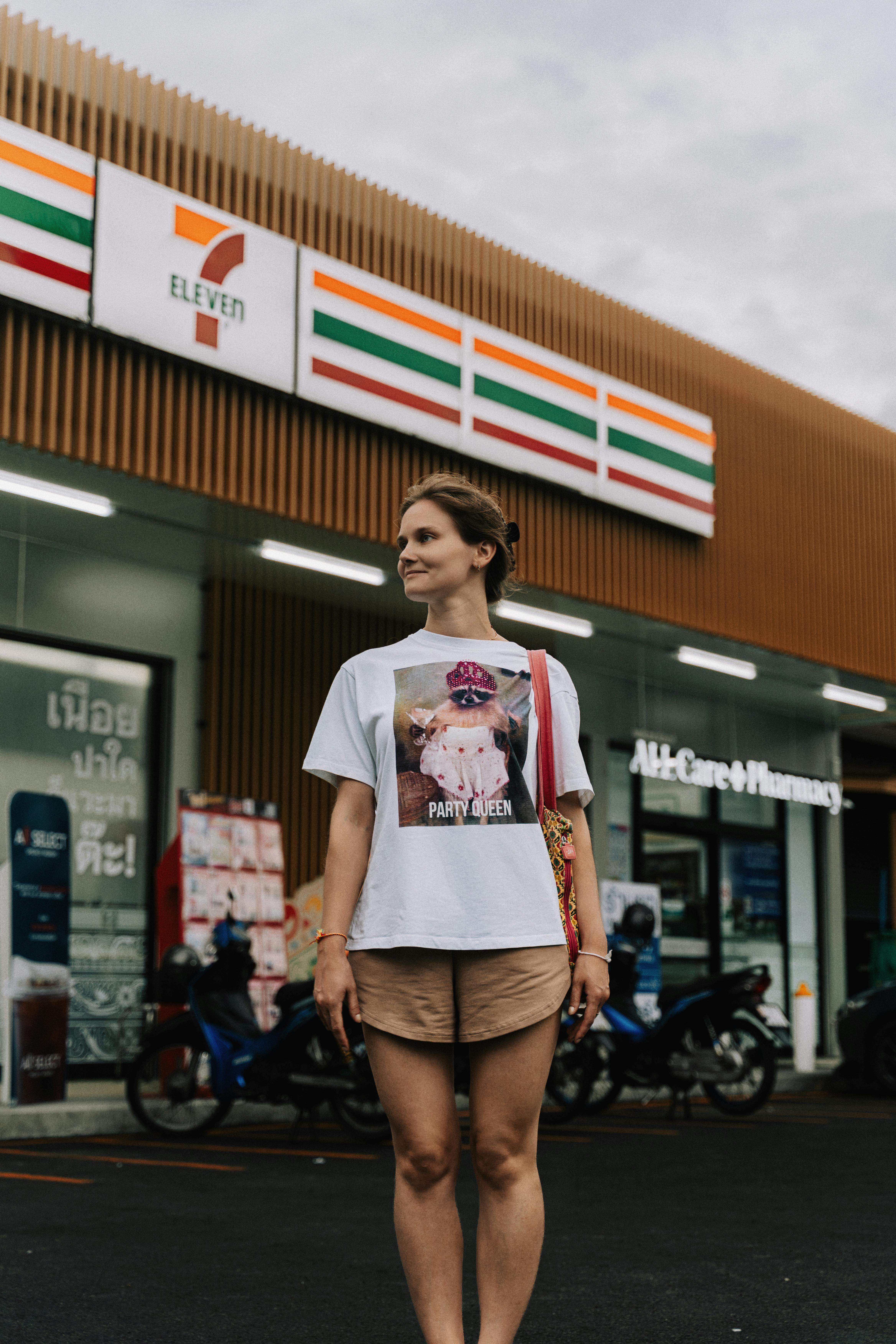 A woman stands outside a 7-Eleven store in Phuket wearing a casual outfit.