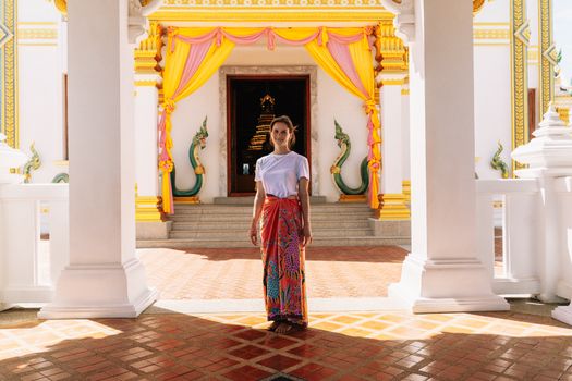 A woman stands in a vibrant temple entrance in Krabi, Thailand, featuring colorful drapery and architecture.