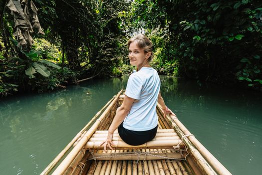 A woman enjoys a serene bamboo raft ride through Krabi's lush green jungle waterways.