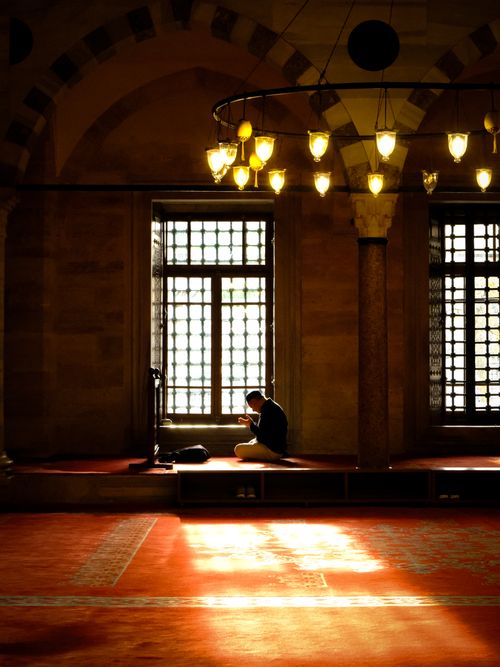 Free Man sitting in prayer at Suleymaniye Mosque in Istanbul with warm lighting and historic architecture. Stock Photo