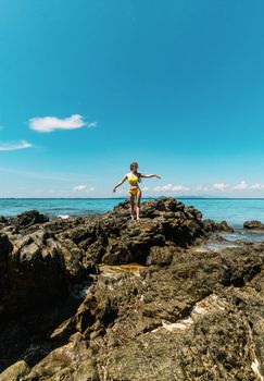 Woman stands on rocks by the clear blue sea in Ao Nang, Krabi, Thailand enjoying a sunny summer day.