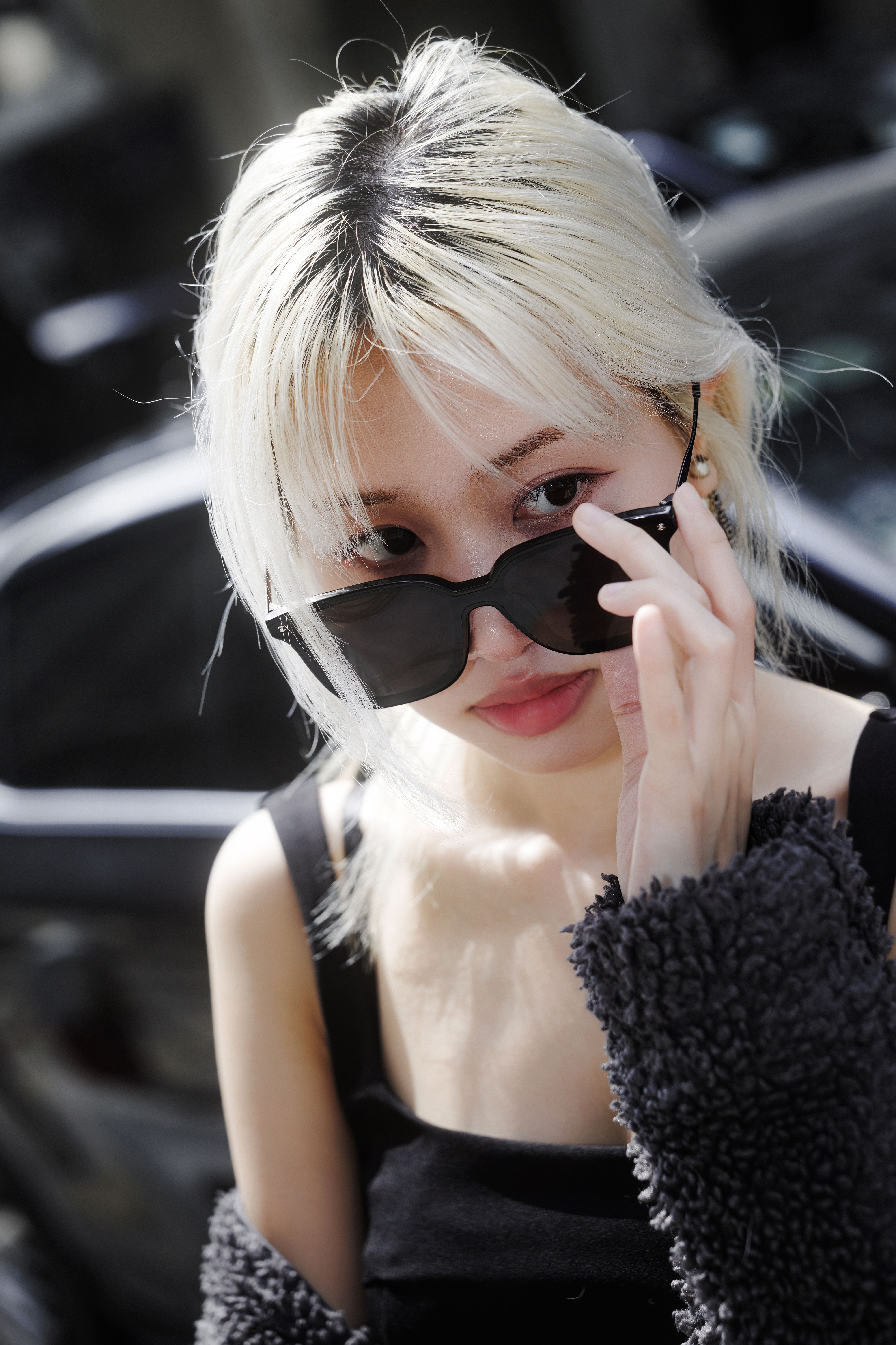 Portrait of a fashionable woman adjusting her sunglasses outdoors, exuding confidence and style.