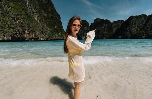 Smiling woman in sunglasses pointing at the scenic Maya Bay in Krabi, Thailand, on a sunny day.