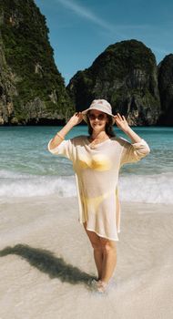 Woman in a hat standing on the beach in Krabi, Thailand, with limestone cliffs in the backdrop.