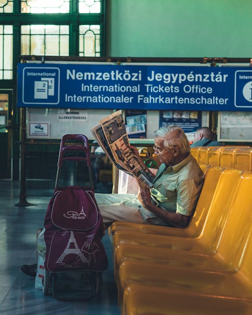 Man Sitting on Gang Chair While Reading a Book