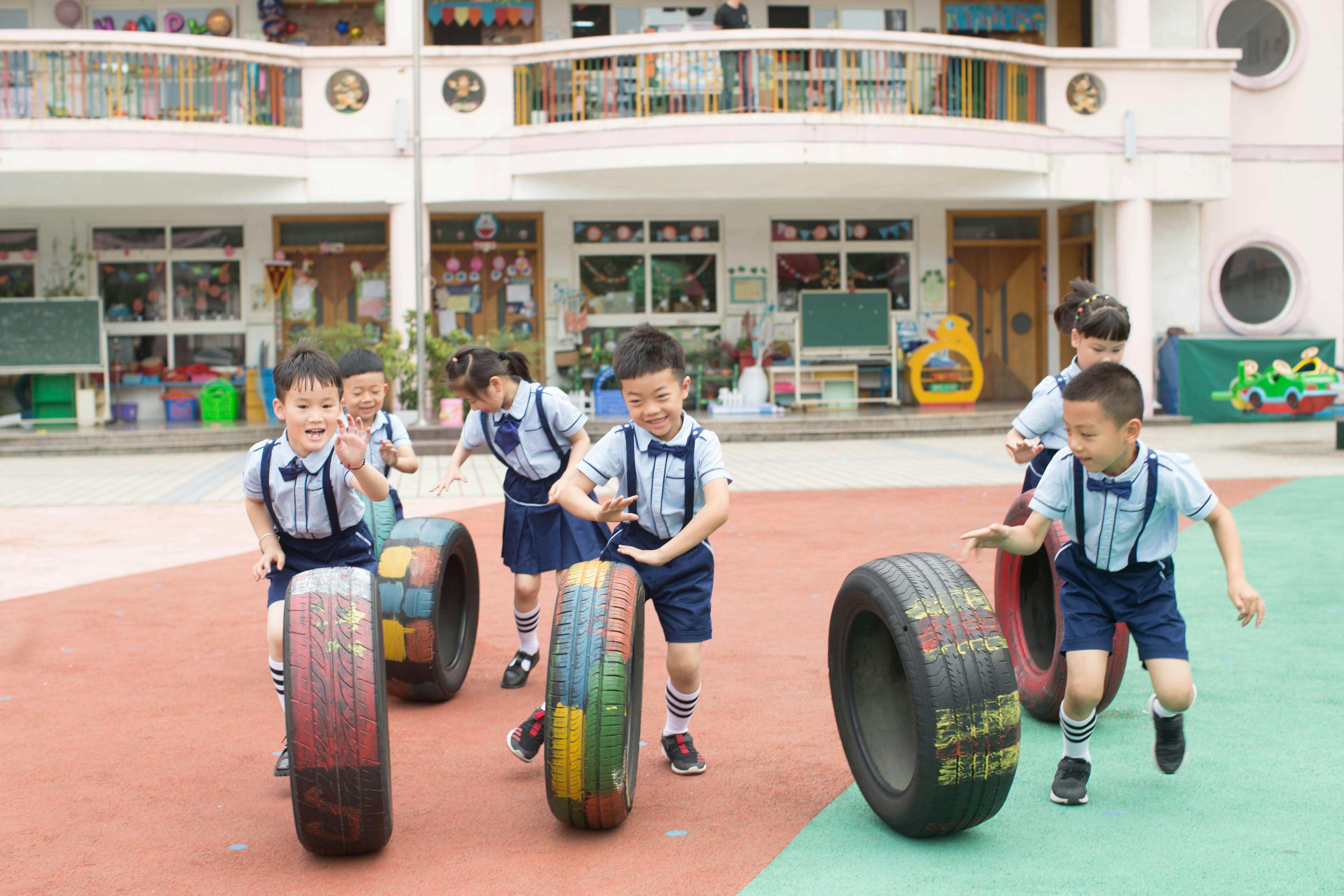 Group of children in uniform playing with painted tires in a school playground.
