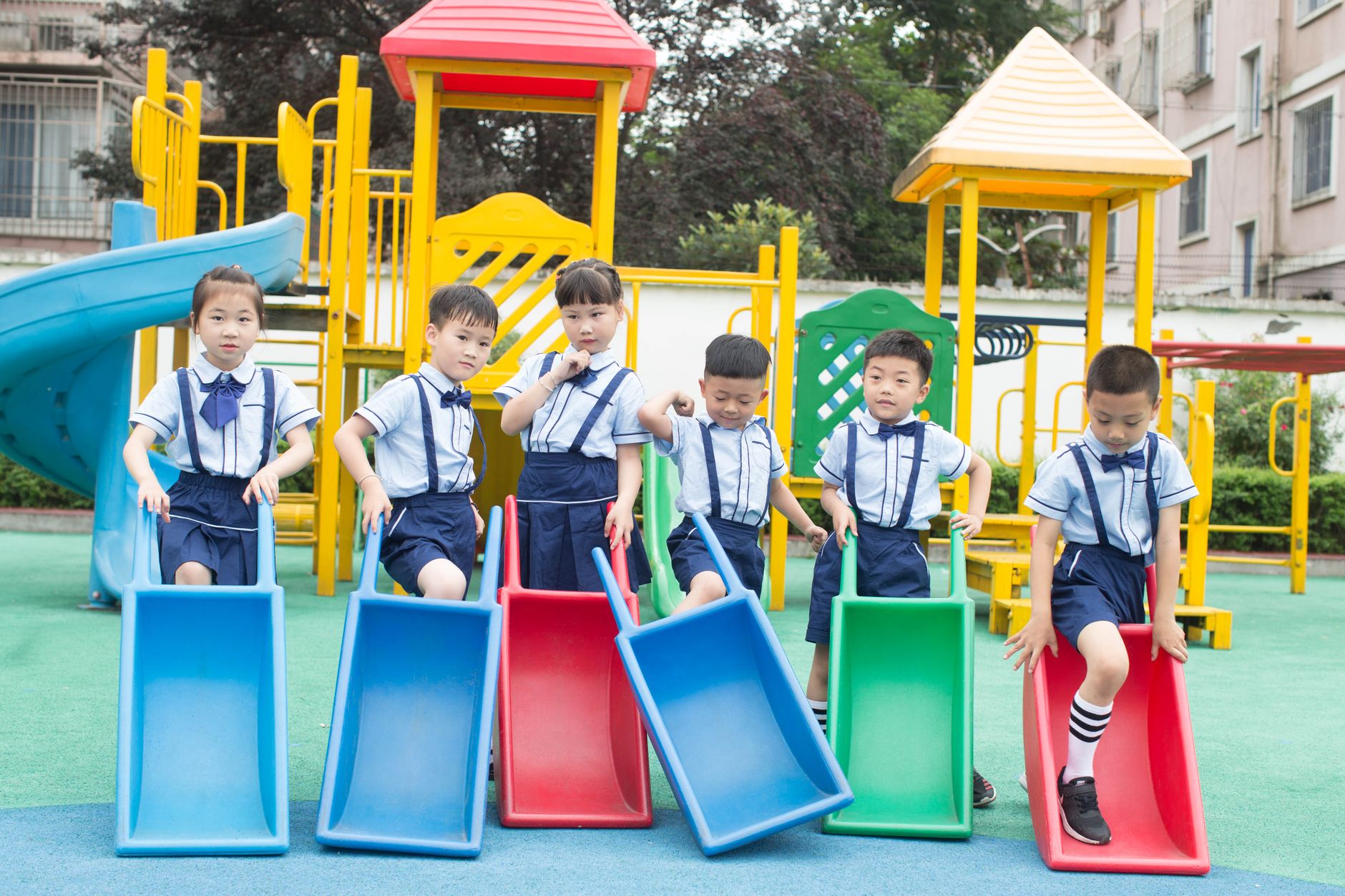 Group of kids in school uniforms playing on vibrant playground slides outdoors.