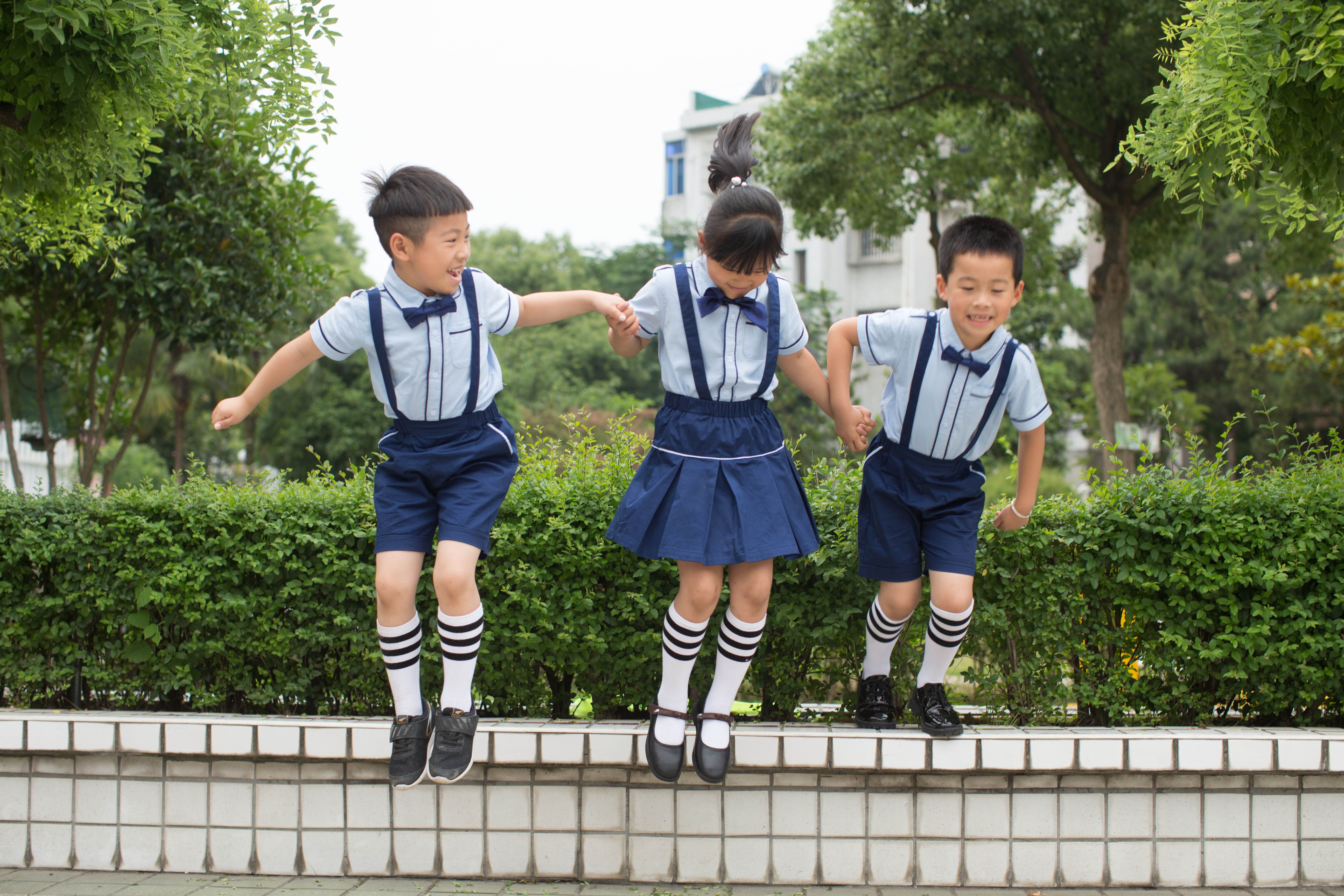 Tiga anak sekolah melompat dengan gembira di luar ruangan